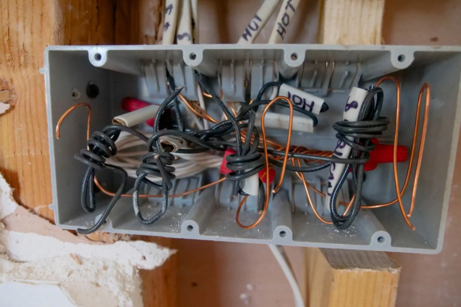En åben samledåse fyldt med ledninger monteret mellem træstolper i en væg under renovering